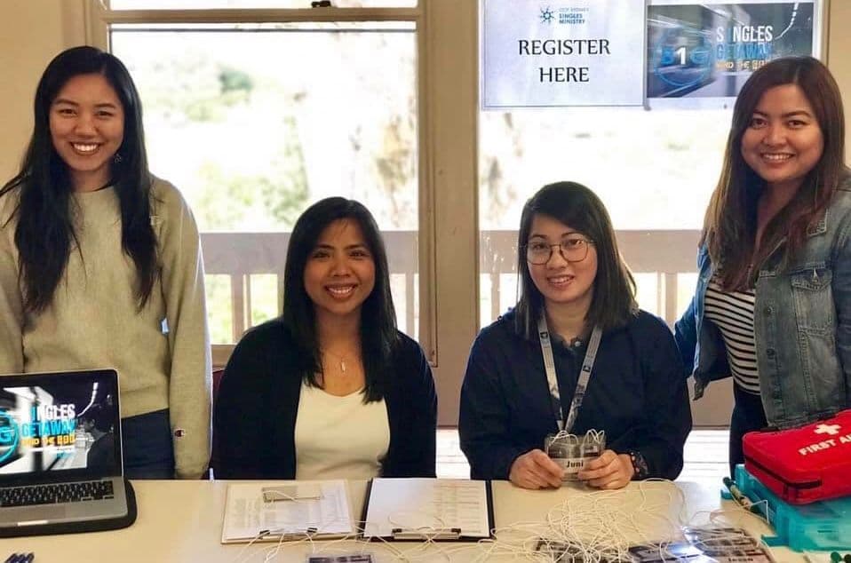 Four people standing behind a welcome table under a sign reading Register Here
